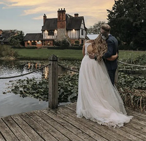The bride and groom look back across the lake at the Moat House Acton Trussell, Staffordshire